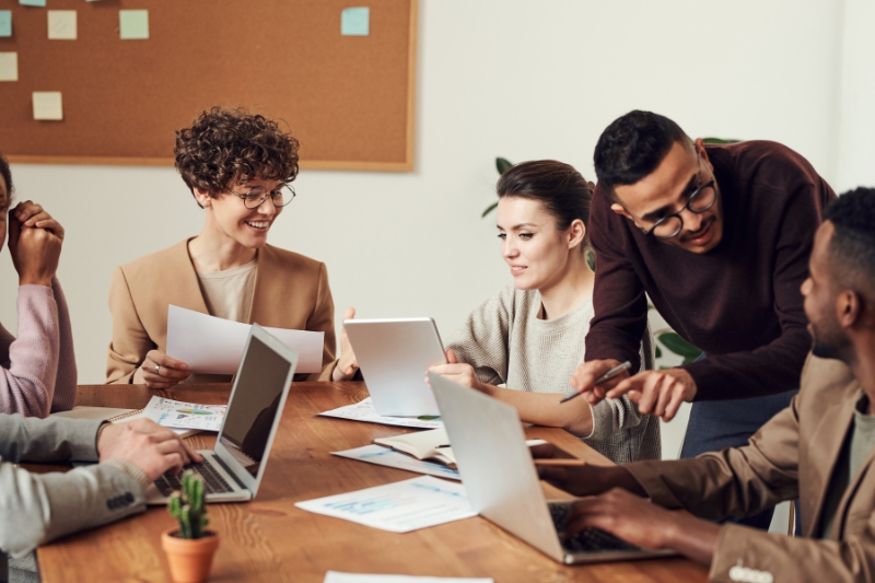 A diverse group of professionals collaborating at a table with laptops in a modern office setting, symbolizing teamwork and creativity in a digital marketing agency in Delhi.